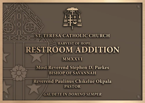 Bronze St. Teresa Catholic Church building addition dedication plaque with a coat of arms, bishop and pastor names, and a Latin motto.