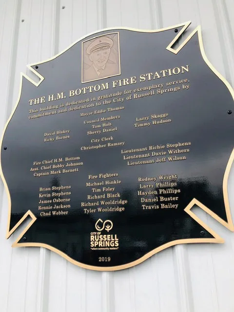 Maltese cross shaped fire station dedication plaque listing the mayor, council, chief, and firefighters