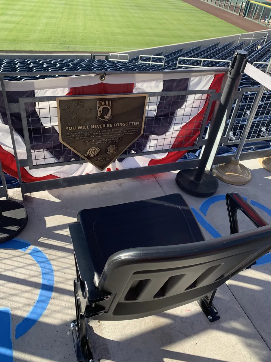 Bronze POW/MIA home plate plaque dedicated at the Reno Aces ballpark on August 3, 2019, mounted above a reserved unoccupied chair overlooking the field