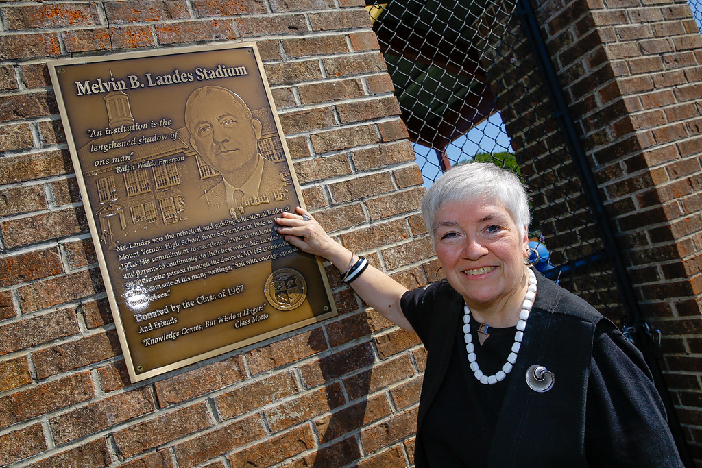 A woman standing next to a new building dedication plaque.