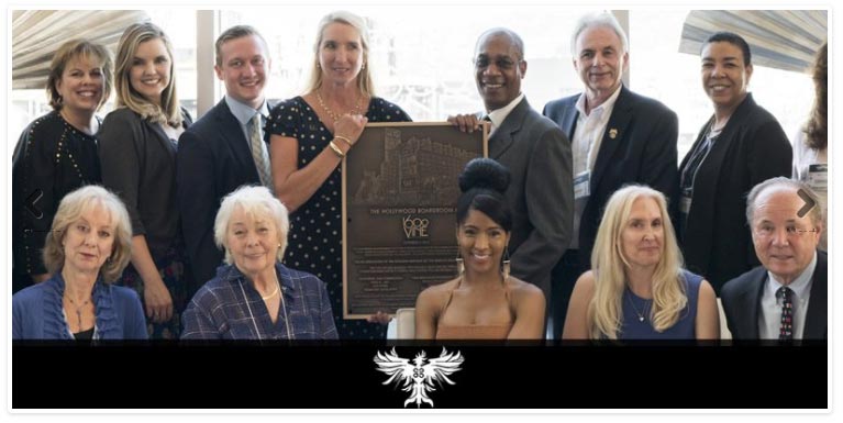 A group of people gather around a bronze plaque at a dedication ceremony.